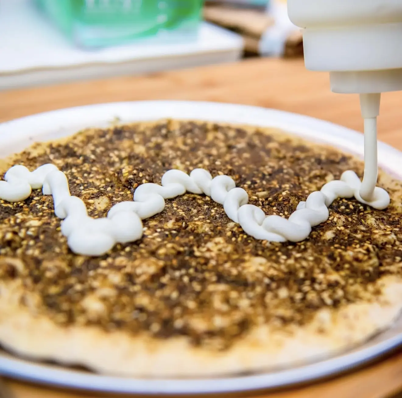 Adding a zigzag of cream on a flatbread with za'atar spread.
