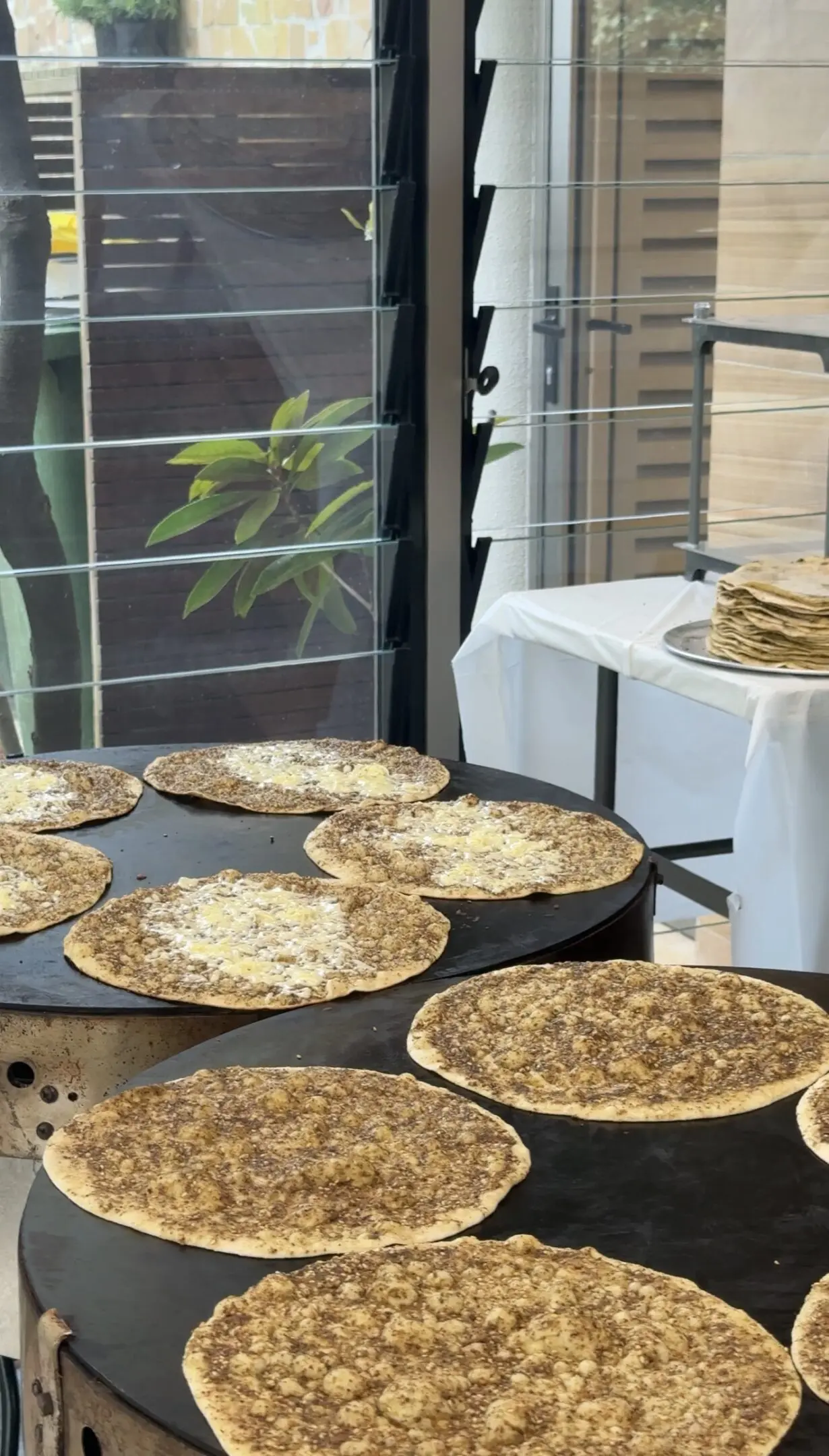 Multiple flatbreads cooking on a large pan beside a stack of similar breads.