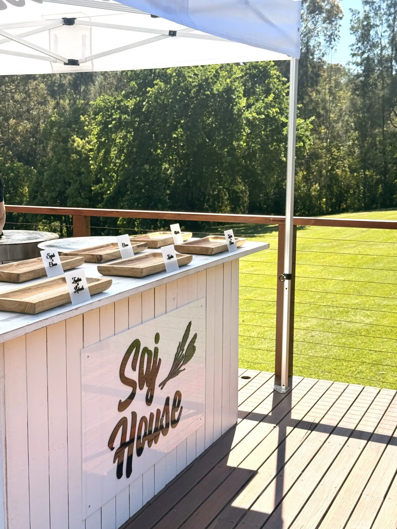 Outdoor bar setup with wooden counter and greenery background.