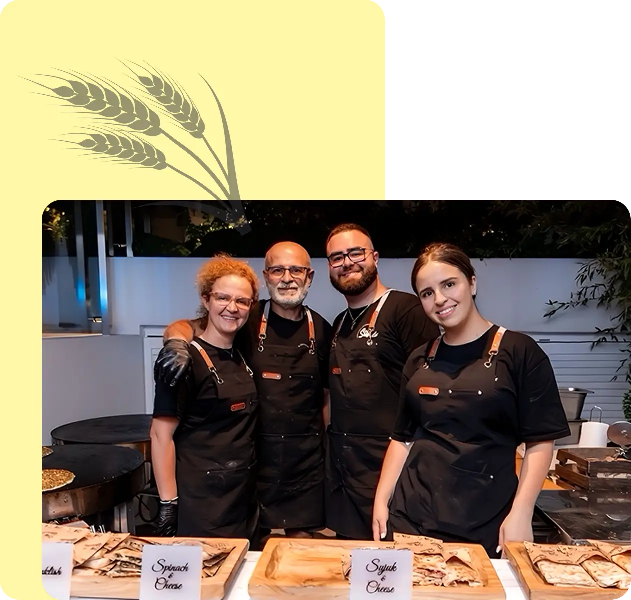 Four smiling chefs stand behind a food stall with various dishes.