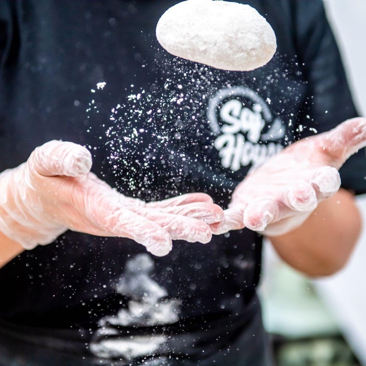 Hands tossing pizza dough in the air, covered with flour.